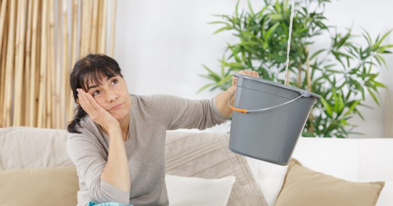 A woman holding a bucket to catch water from a leaky roof.